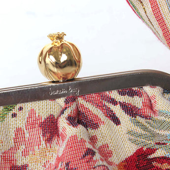 Close-up of a floral clutch with a gold pomegranate clasp on a light blue background