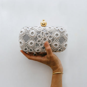 White crocheted clutch bag with a gold clasp on a white background