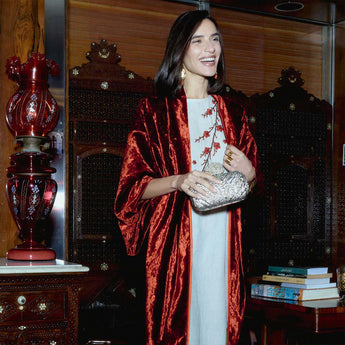 Woman in a red velvet kimono holding a clutch in an indoor setting with decorative elements.