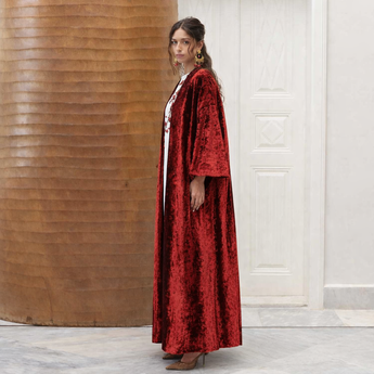 Woman wearing a red velvet robe over a white vanda with floral patterns, standing against a wooden wall.