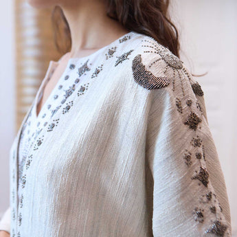 Close-up of a person wearing a white outfit with intricate silver embroidery on a blurred background