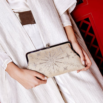 A model holding a gold clutch bag with a metallic sun and stars pattern, and a silver clasp.