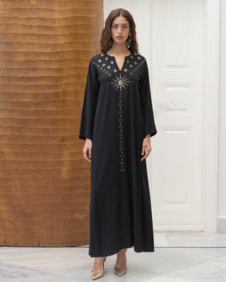 Woman wearing a black dress with intricate rising sun designs in a room with wooden and white walls.