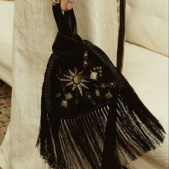 Black hand beaded slip bag with fringes held by a person wearing a long beige garment.