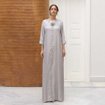 Woman wearing a long silver panda with a rising sun embroidery in a minimalistic setting