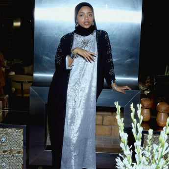 Woman in a black abaya and silver vanda traditional outfit standing indoors with a metallic wall background.