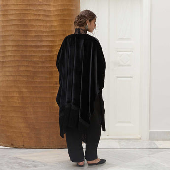 Woman wearing a black velvet poncho in a minimalistic setting.