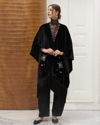 Woman wearing a black velvet poncho with embroidered sunrise details in a minimalistic setting.