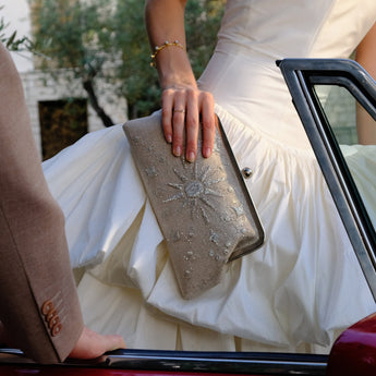 Person holding a silver clutch beaded in the shape of a sun