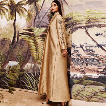 A person wearing a gold cover up with a rising sun sleeve design, standing in a room with a tropical-themed mural.