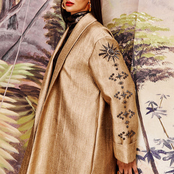 A person wearing a gold cover up with a rising sun sleeve design, standing in a room with a tropical-themed mural.