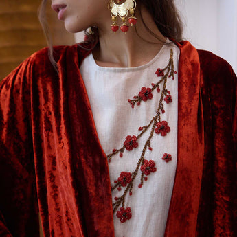 Person wearing a red velvet kimono over a vanda with embroidered floral patterns.