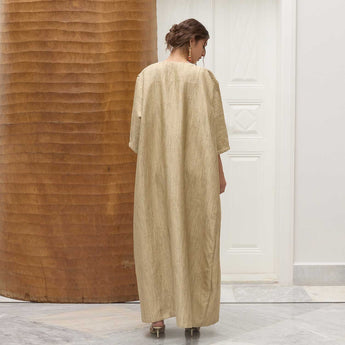 Woman wearing a beige long abaya standing in a room with wooden and white walls.