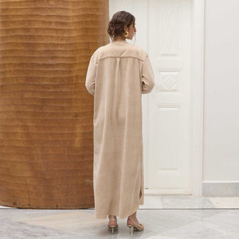 Woman wearing a beige long Amira dress standing in a room with wooden and white walls.