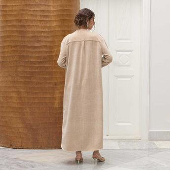 Woman wearing a long beige coat standing in a room with wooden and white walls.