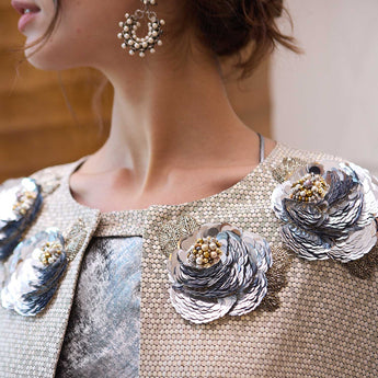 Close-up of a person wearing a decorative cape with floral embellishments and pearl earrings.