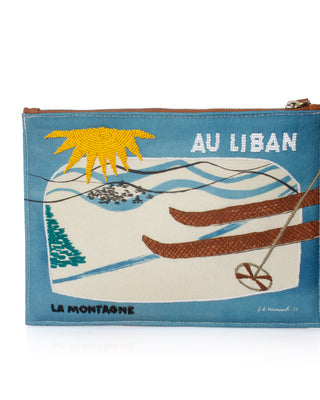 A rectangular zippered pouch with a blue border and a vintage-style ski illustration. The design features a yellow sun, green pine tree, white snow, brown skis, and the text 'AU LIBAN' and 'LA MONTAGNE'.