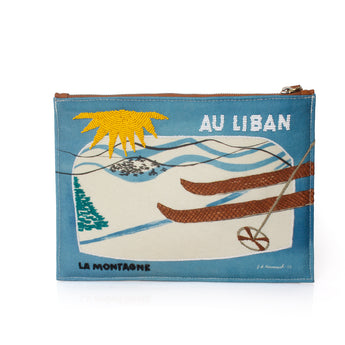 A rectangular zippered pouch with a blue border and a vintage-style ski illustration. The design features a yellow sun, green pine tree, white snow, brown skis, and the text 'AU LIBAN' and 'LA MONTAGNE'.