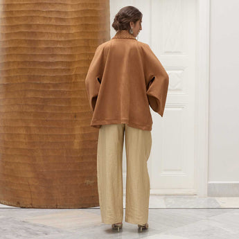 Woman wearing a brown smocking jacket and beige pants in an indoor setting.
