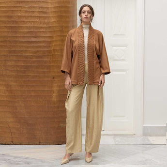 Woman wearing a brown smocking jacket and beige pants in an indoor setting.