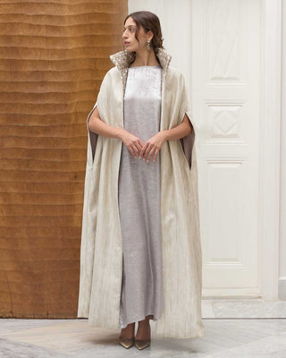 Woman in a long, light-colored imperial cape with a matching vanda standing against a wooden wall.