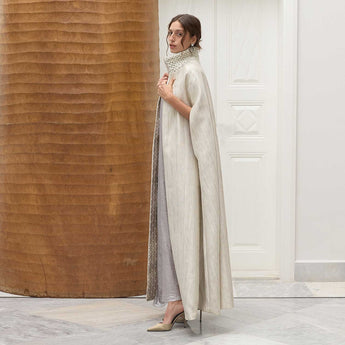 Woman in a long, light-colored imperial cape with a matching vanda standing against a wooden wall.