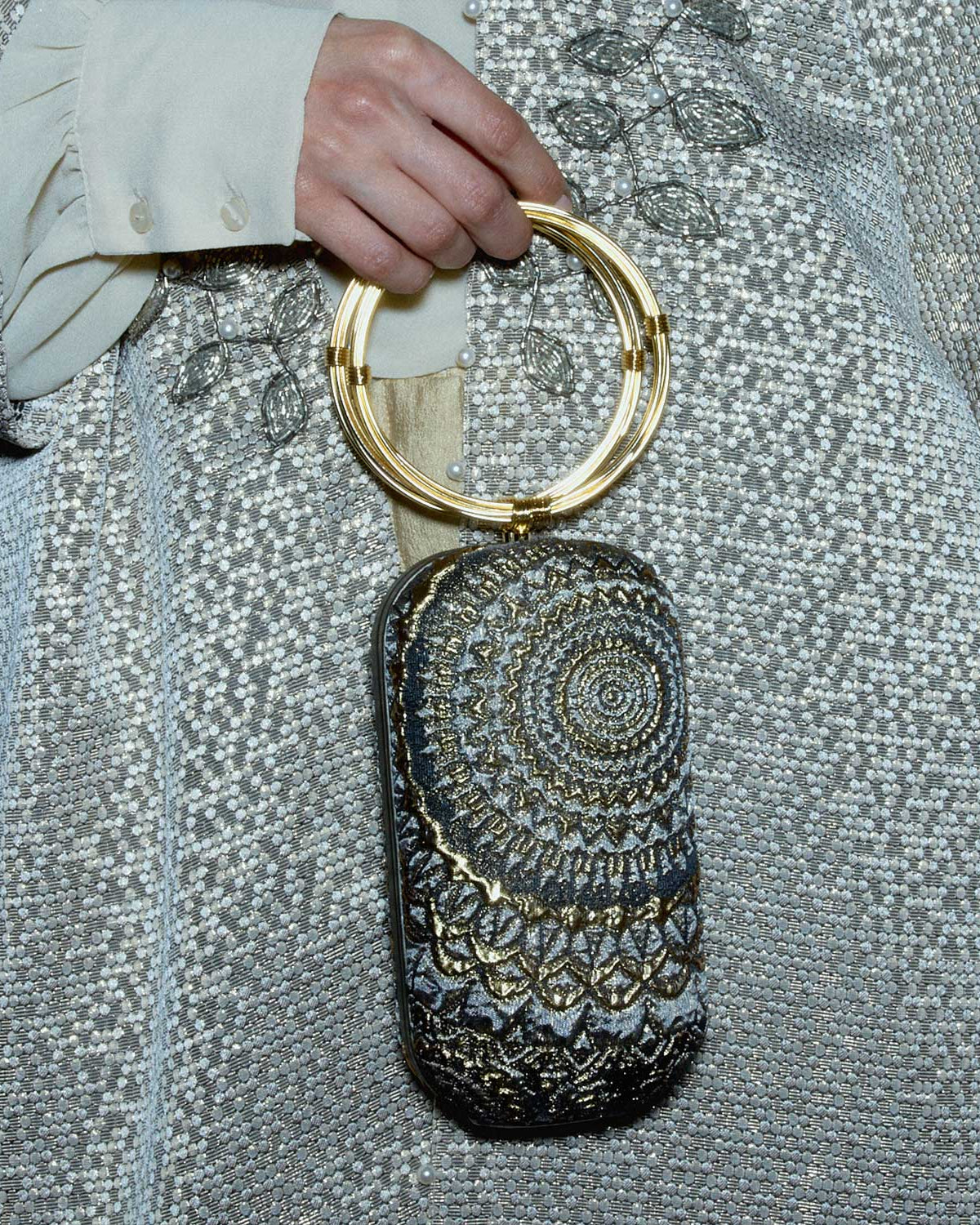 Bracelet bag sunburst pattern with gold ring wristlet held by a person wearing a silver sequin outfit.