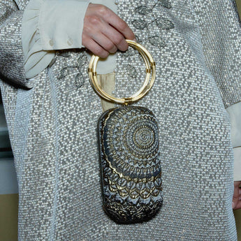 Menottes sunburst pattern with gold ring handle held by a person wearing a silver sequin outfit.