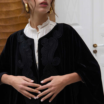 close up of a woman wearing a black embroidered poncho over a white shirt.