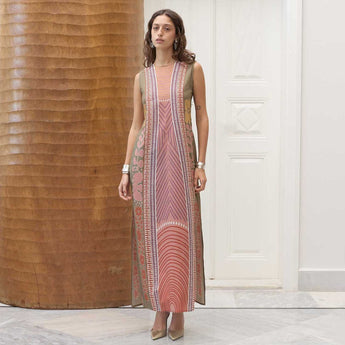 Woman wearing a long, patterned vanda dress standing in a room with wooden and white walls.