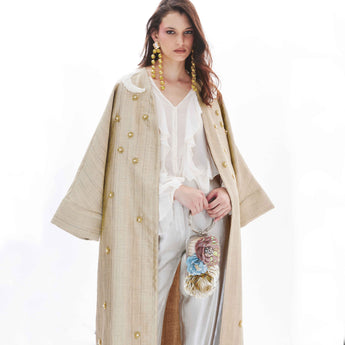 Woman wearing a gold abaya embroidered with stars and two moon over a white dress on a white background