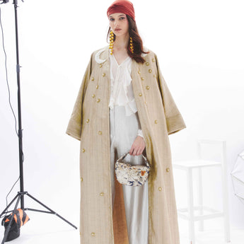 Woman wearing a gold abaya embroidered with stars and two moon over a white dress on a white background