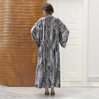 Woman wearing a long, velvet kimono beaded with a moon over a plain dress in a minimalistic setting.