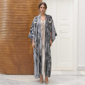 Woman wearing a long, velvet kimono beaded with a moon over a plain dress in a minimalistic setting.