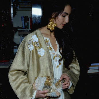 Gold seashell earrings worn by a person with a neutral background