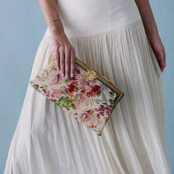 Person holding a floral clutch in front of a plain background